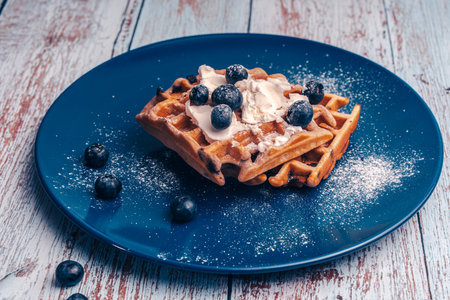 Belgian waffles with blueberries sprinkled with powdered sugar on a plate. High quality photoの写真素材