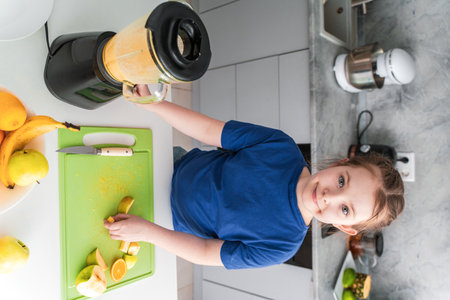 Cute little girl making fruit cocktail in the kitchen. Happy pre-teen girl putting fruit in blender. Selected Focus. High quality photoの写真素材