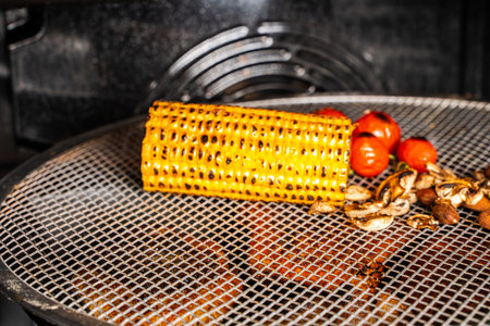 Vegetables are baked in the oven. Corn, cherry tomatoes and mushrooms on a steel rack in the oven. High quality photoの写真素材