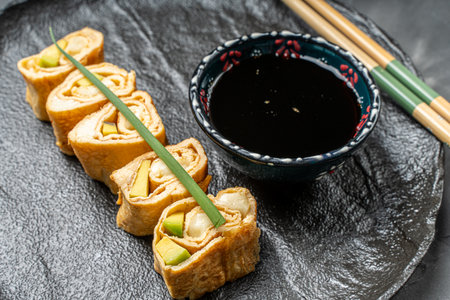 Tamagoyaki or a traditional Japanese omelet roll with avacado and cheese on a black mica plate with soy sauce and chopsticks. High quality photoの写真素材