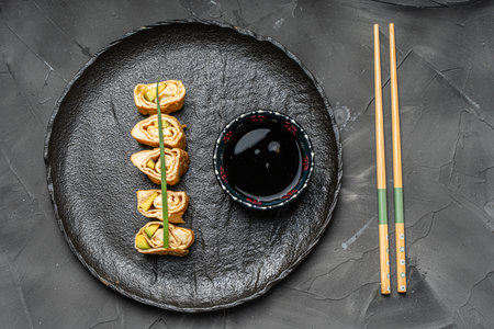 Tamagoyaki or a traditional Japanese omelet roll with avocado and cheese on a black plate with soy sauce and chopsticks. High quality photoの写真素材