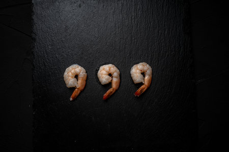 Three boiled, frozen shrimp on a black mica board, laid out in a row. Place for text. High quality photoの写真素材