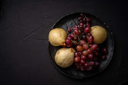 Clusters of red grapes and yellow pears on a black mica plate on a dark background. Space for text. High quality photoの写真素材