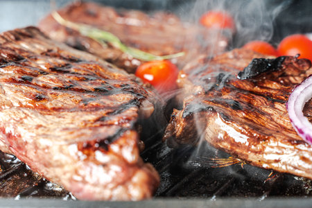 Meat or steak is grilled with cherry tomatoes and rosemary. The process of cooking steak. Close-up. High quality photoの写真素材