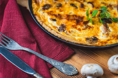 Quiche or pie with meat, chicken and mushrooms on a wooden table with cutlery, herbs and cherry tomatoes. High quality photoの写真素材
