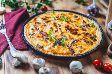 Quiche according to a traditional French recipe. Pie with chicken and mushrooms on a plate on a wooden background with cutlery and a napkin. High quality photoの写真素材