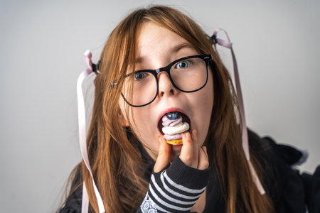 A little girl, a pre-teenager holding a cake in her hands and looking at it smiling, she is dressed in black and white clothes and black eye glasses on a gray background. High quality photoの写真素材