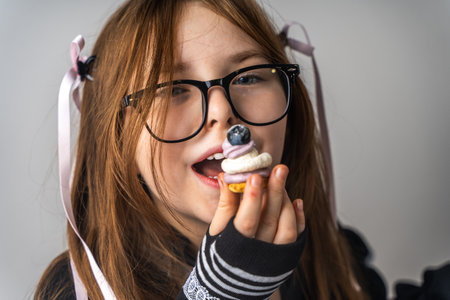 A pretty little girl, a pre-teenager holding a cake in her hands and looking at it smiling, she is dressed in black and white clothes on a gray background. High quality photoの写真素材