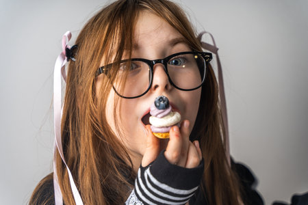 A pretty little girl, a pre-teenager holding a cake in her hands and looking at it smiling, she is dressed in black and white clothes on a gray background. High quality photoの写真素材
