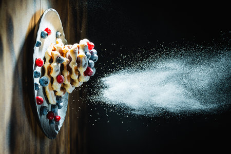 Belgian waffles with blueberries and cranberries sprinkled with powdered sugar on a black background on a wooden table. Space for text. High quality photoの写真素材