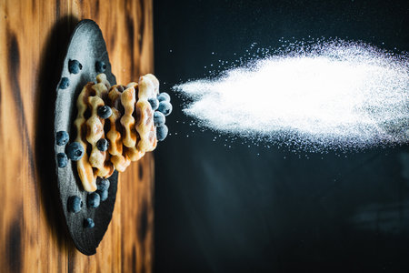 Belgian waffles with blueberries, sprinkled with powdered sugar. Waffles with berries on a black...
