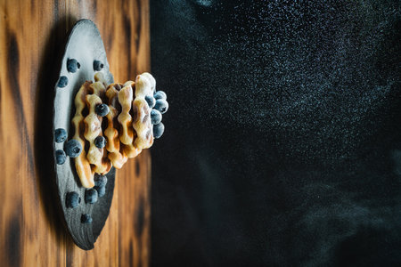 Belgian waffles with blueberries, sprinkled with powdered sugar. Waffles with berries on a black background on a wooden table. High quality photoの写真素材