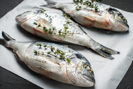 Three raw fresh fish dorado on baking paper on a black background. View from above. High quality photoの写真素材