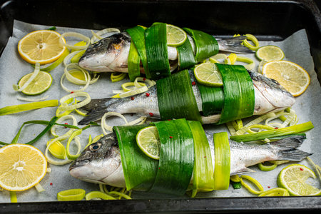 Dorado fish wrapped in leek leaves with lemon and lime with onion rings cut on baking paper in a baking tray. High quality photoの写真素材