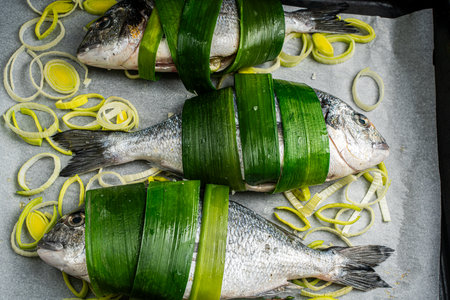Raw, fresh dorado fish on baking paper wrapped in leek leaves with onions cut into rings. High quality photoの写真素材
