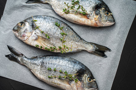 Three raw fresh fish dorado on baking paper on a black background. View from above. High quality photoの写真素材