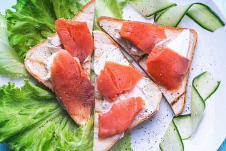 Sandwiches with cottage cheese and slices of salted trout on a white plate with cucumber and herbs. High quality photoの写真素材