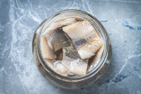 Pieces of marinated herring in a glass jar on a gray marble table. High quality photoの写真素材