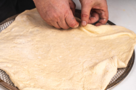 Mens hands stretching yeast pizza dough on a white table. The process of making a pizza or pie. High quality photoの写真素材