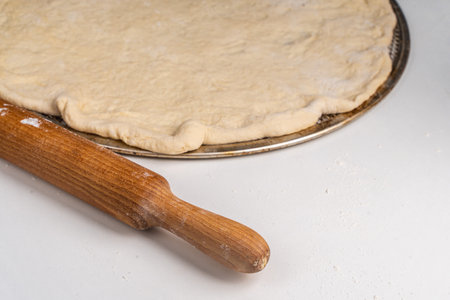 Rolled out pizza dough on a rolling pin on a white table. Pizza cooking process, recipe. High quality photoの写真素材