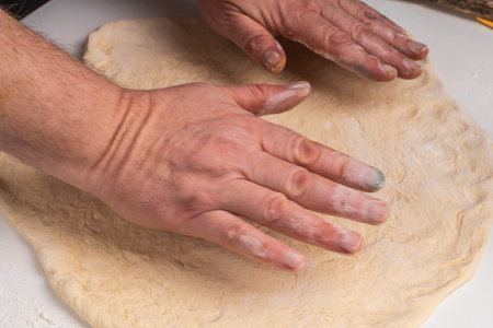 Mens hands stretching yeast pizza dough on a white table. The process of making a pizza or pie. High quality photoの写真素材