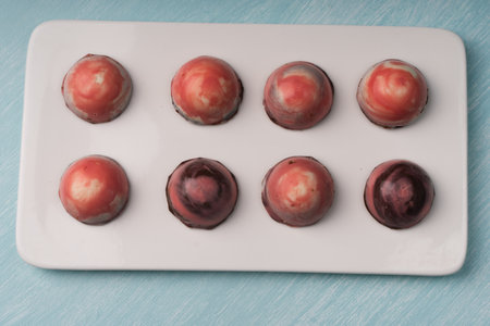 Assorted multi-colored homemade chocolates. Modern hand-painted chocolates on a white plate on a...