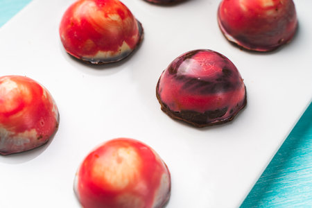 Assorted multi-colored homemade chocolates. Modern hand-painted chocolates on a white plate on a...