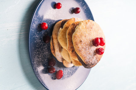 Cottage cheese pancakes with cranberries are stacked on a blue plate on a light blue table,...