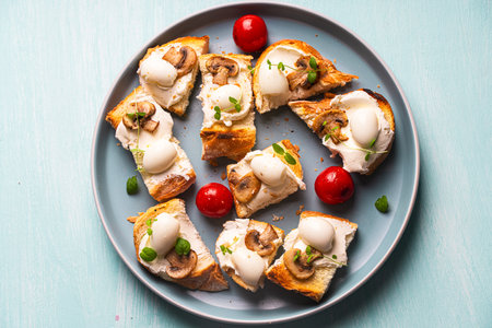 Mini toast with cottage cheese, quail eggs, cherry tomatoes, mushrooms and microgreens on a blue plate. Copyspace. High quality photoの写真素材