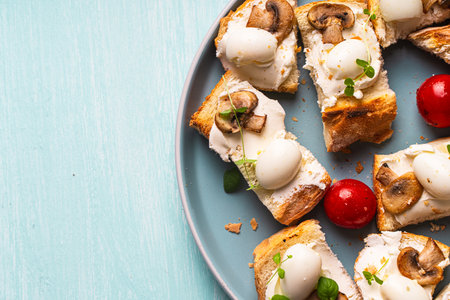 Mini toast with cottage cheese, quail eggs, cherry tomatoes, mushrooms and microgreens on a blue plate. Copyspace. High quality photoの写真素材