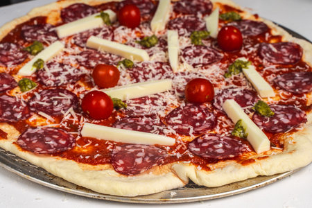 Pizza is prepared for baking. Raw pepperoni pizza with sausage, mozzarella cheese, cherry tomatoes and basil on a baking wheel. High quality photoの写真素材