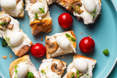 Mini toast with cottage cheese, quail eggs, cherry tomatoes, mushrooms and microgreens on a blue plate. High quality photoの写真素材