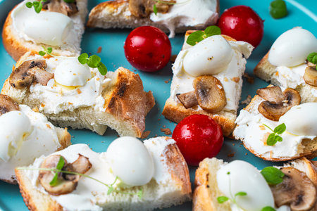 Mini toast with cottage cheese, quail eggs, cherry tomatoes, mushrooms and microgreens on a blue plate. High quality photoの写真素材