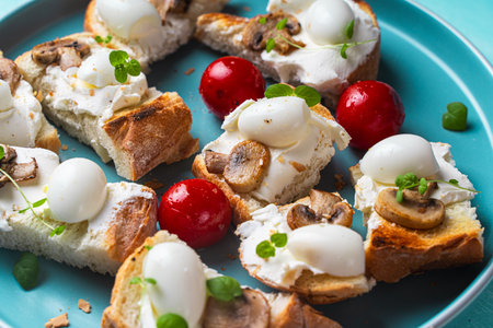 Mini toast with cottage cheese, quail eggs, cherry tomatoes, mushrooms and microgreens on a blue plate. High quality photoの写真素材