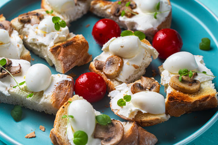 Mini toast with cottage cheese, quail eggs, cherry tomatoes, mushrooms and microgreens on a blue plate. High quality photoの写真素材