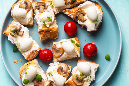 Mini toast with cottage cheese, quail eggs, cherry tomatoes, mushrooms and microgreens on a blue plate. High quality photoの写真素材