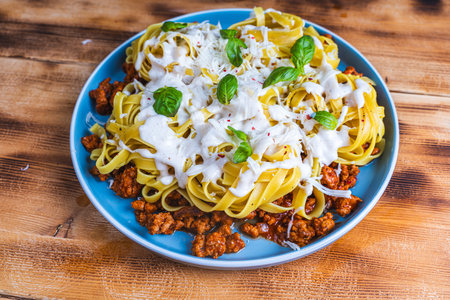 Spaghetti Bolognese pasta nests with Bechamel sauce and minced beef fried with tomatoes, onions and carrots on a blue plate on a wooden table. Top view. Copyspace or space for text. High quality photoの写真素材