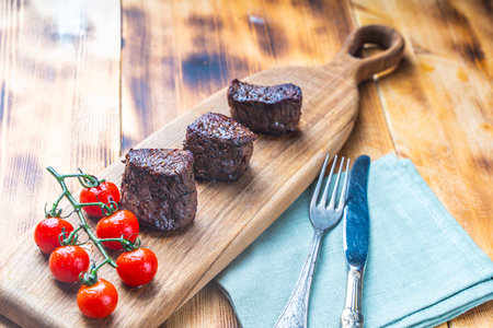 Filet mignon, beef steaks on a wooden board with cherry tomatoes with a napkin and cutlery on the table. High quality photoの写真素材