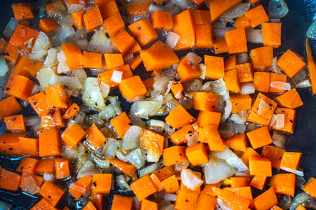 Diced carrots and onions are fried in a pan. Background with the texture of roasted vegetables. High quality photoの写真素材