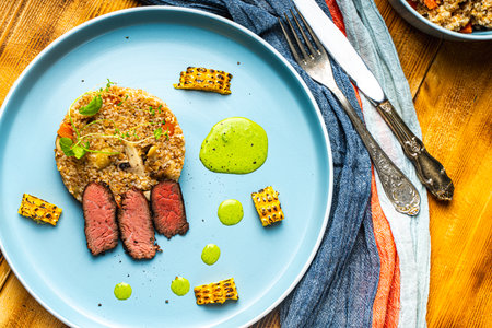 Sliced filet mignon steak with grits, mushrooms and corn served on a blue plate with a napkin and cutlery on a wooden background. Close-up. High quality photoの写真素材