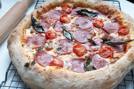 Raw pepperoni pizza is ready to cook. Pizza with sausage, tomatoes, cheese and basil on a baking rack. High quality photoの写真素材