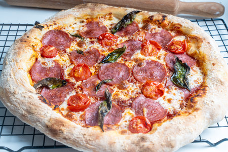 Raw pepperoni pizza is ready to cook. Pizza with sausage, tomatoes, cheese and basil on a baking rack. High quality photoの写真素材