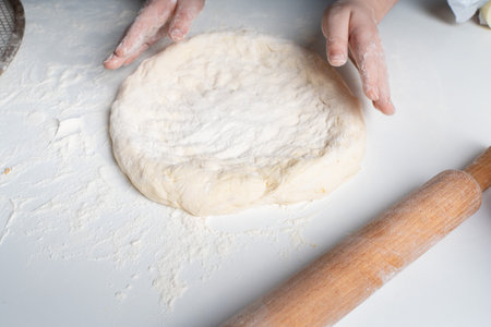 The hands show a circle of dough on a white table. The concept of cooking and hobbies. High quality photoの写真素材