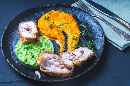Chicken Cordon Bleu with carrot puree and spinach mashed potatoes on a black board top view. A traditional French dish in an original presentation. Healthy eating and diet concept. High quality photoの写真素材