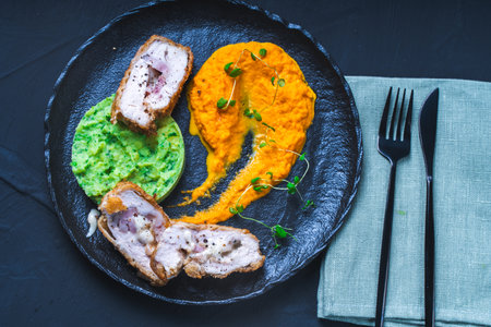 Chicken Cordon Bleu with carrot puree and spinach mashed potatoes on a black board top view. A traditional French dish in an original presentation. Healthy eating and diet concept. High quality photoの写真素材