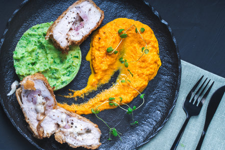 Chicken Cordon Bleu with carrot puree and spinach mashed potatoes on a black board top view. A traditional French dish in an original presentation. Healthy eating and diet concept. High quality photoの写真素材