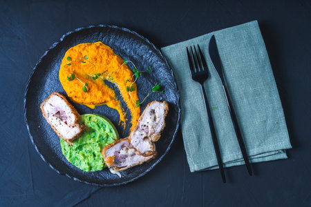 Chicken Cordon Bleu with carrot puree and spinach mashed potatoes on a black board top view. A traditional French dish in an original presentation. Healthy eating and diet concept. High quality photoの写真素材