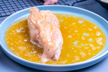 Chicken meat rolled in flour is dipped in egg yolk in a blue plate. High quality photoの写真素材