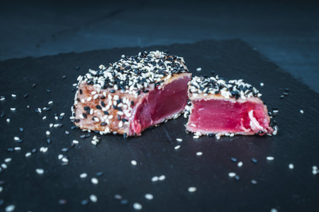 Tuna fried with black and white sesame seeds on a dark mica board on a gray background. Tuna fish steak. Restaurant serving, healthy food. High quality photoの写真素材