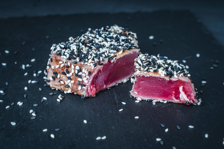 Tuna fried with black and white sesame seeds on a dark mica board on a gray background. Tuna fish steak. Restaurant serving, healthy food. High quality photoの写真素材